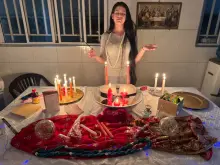 Melissa de olhos fechados diante de uma mesa com velas acesas, velas em forma de casal, um coração, perfume e guias azuis